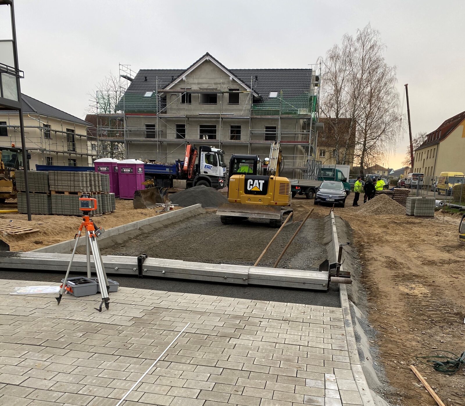 EMC-Baustelle mit Minibagger, Rotationslaser und frisch verlegtem Pflaster vor einem Neubau